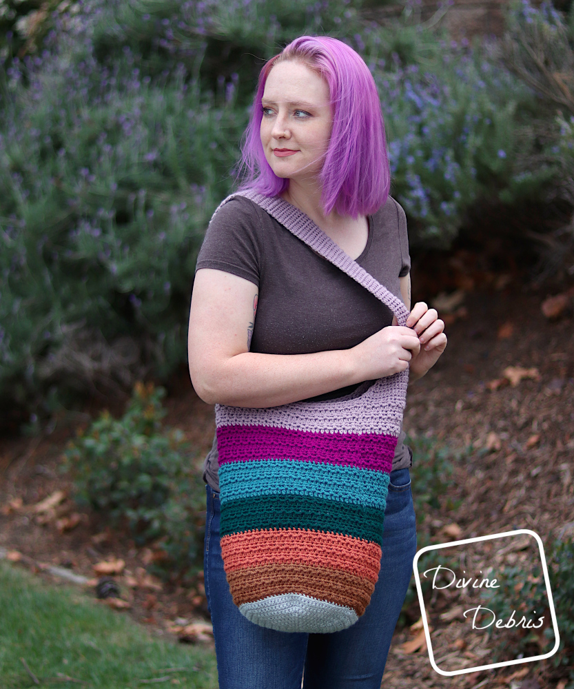[image description] White woman with purple hair looks to the left while holding the strap of the striped Alix Bag, pulling it across her body.