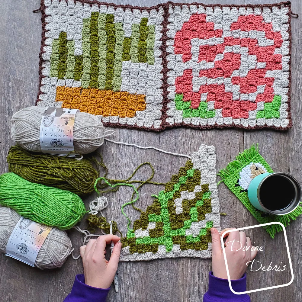 [Image description] C2C Monstera Leaf Afghan Square on the bottom with hands holding it, 4 skeins of yarn to the left in the center, the finished C2C Cactus Square and finished C2C Rose Square on top.