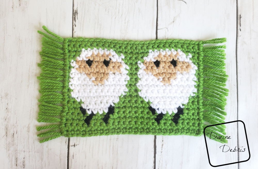 [image description] Simple rectangular sheep design, white sheep on a green background, with fringe on the side. The Dancing Sheep Mug Rug 