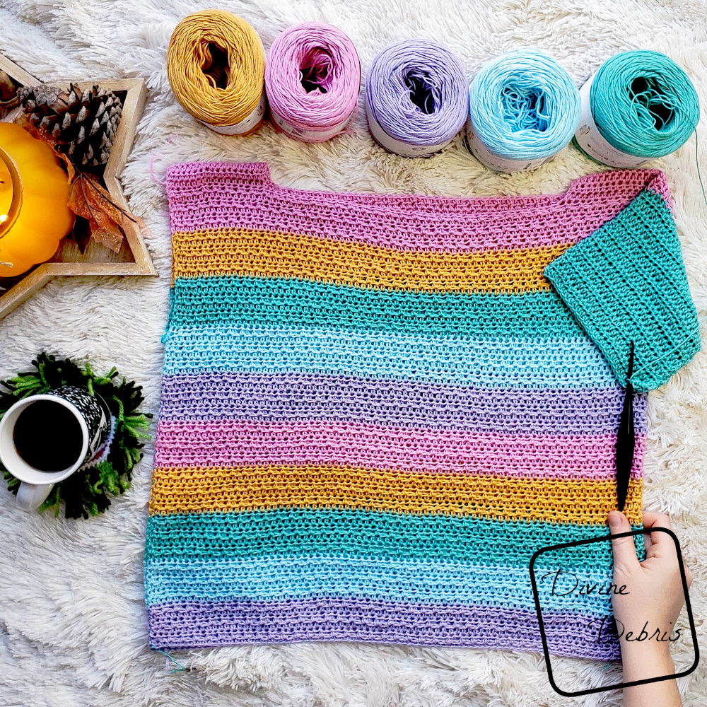 [Image description] Unfinished striped Alix Pullover lays on a white background with a hand holding the right bottom edge and a cup of coffee on the left side