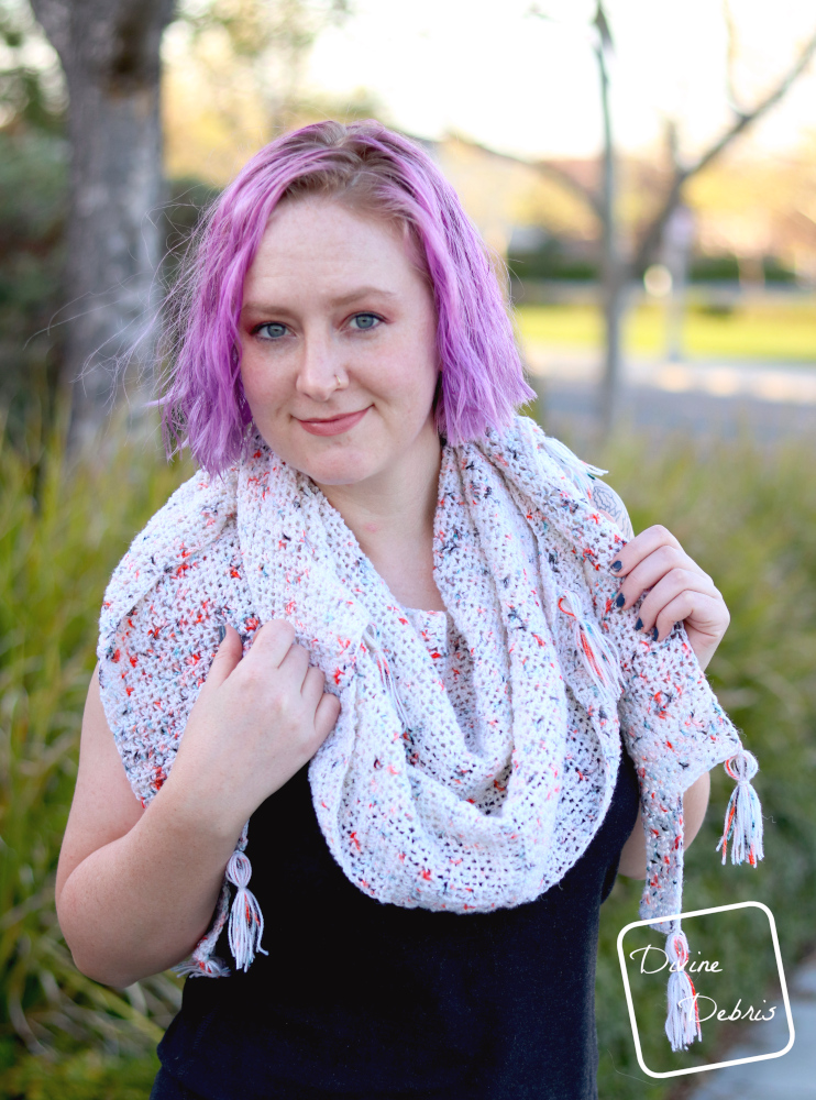 [image description]White woman with purple hair smiles at the camera while wearing Lois Shawl wrapped around her neck, holding onto it with both hands