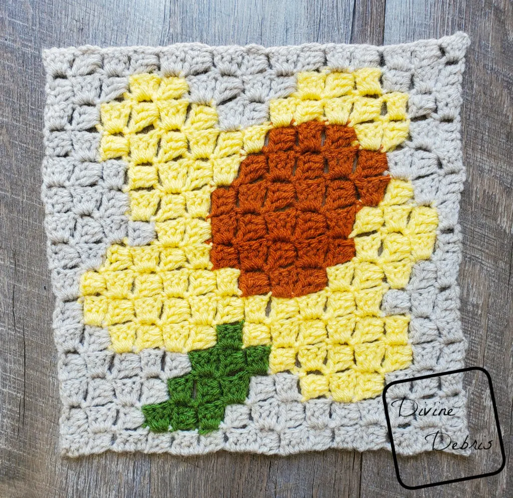 [Image description] C2C Daffodil Afghan Square laying in the center of the frame on a wood-grain background. 