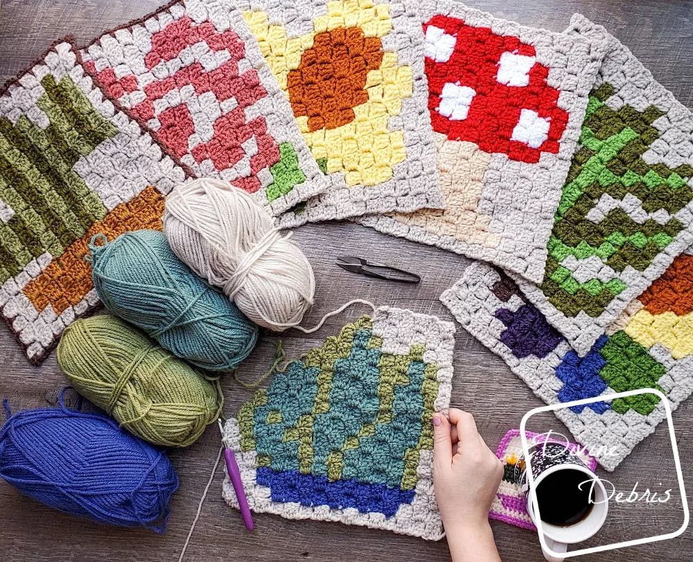 [Image description] the C2C Agave Square lays half-finished flat on a wood grain background, a white woman's hand holds the bottom right corner, 4 skeins of yarn sit on the left and a fan of the previous c2c squares around the top of the photo