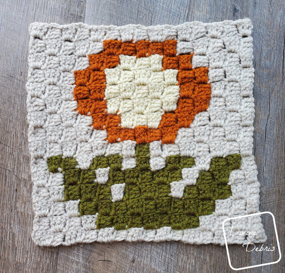 [Image description] the C2C Mum Afghan Square lays flat in the center of the photo on a wood-grain background.