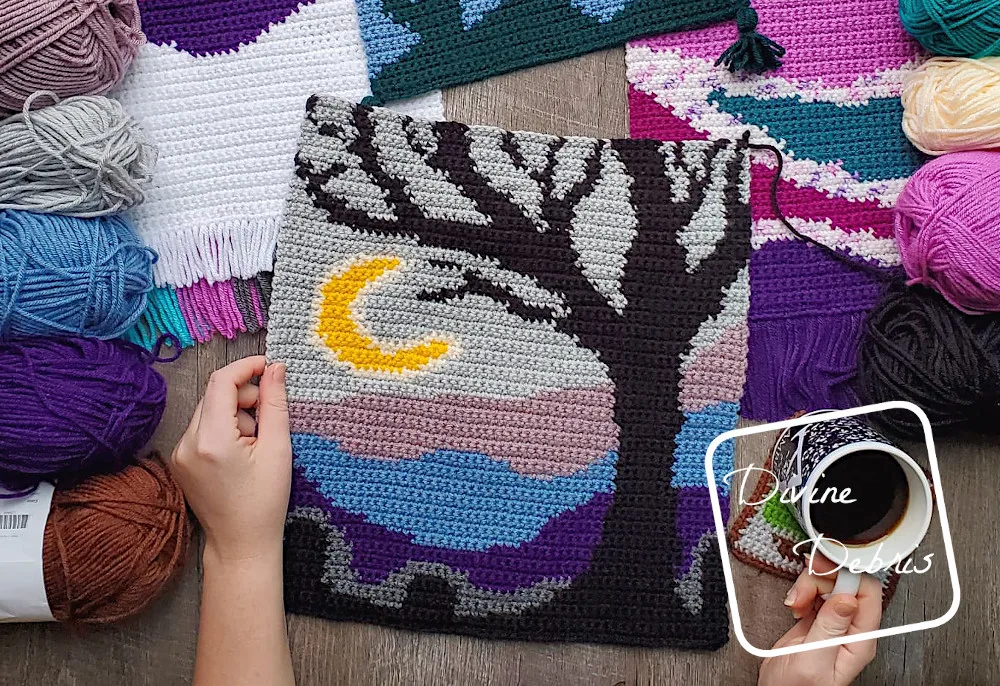 [Image description] A white woman's left had holds and unfinished Cool Tree Wall-Hanging in the center of the photo. Portions of other wall-hangings and skeins of yarn can be partially seen around the edges of the photo.