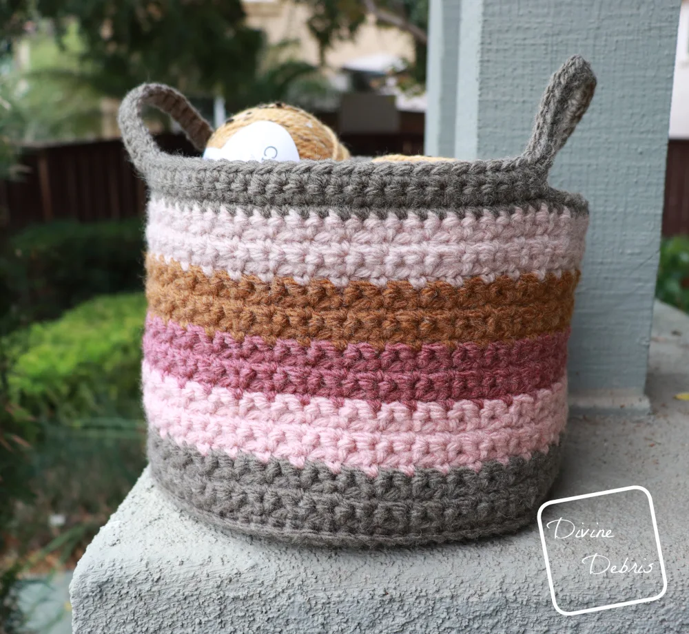 [image description] Amelia Basket crochet pattern with a couple skeins of yarn in side, sitting on a grey platform and bushes on the left side of the photo
