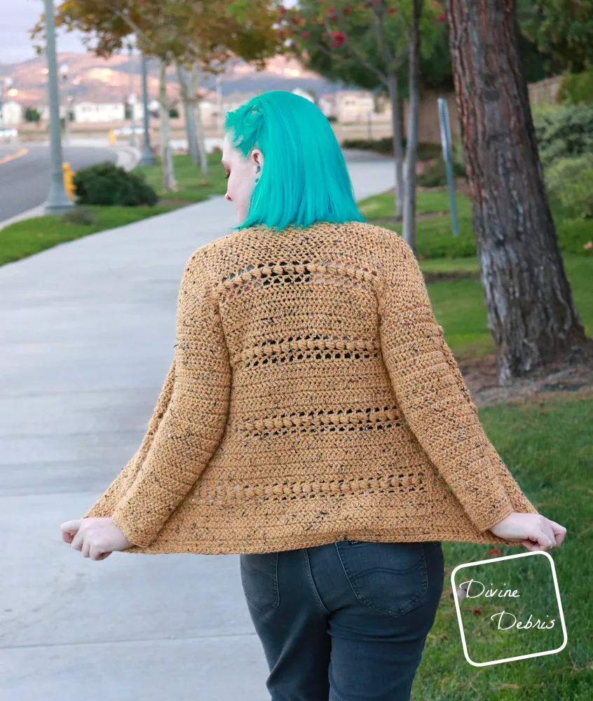[Image description] A white woman with blue hair stands facing away from the camera in front of a tree and grass in the yellow tweed Loretta Cardigan 