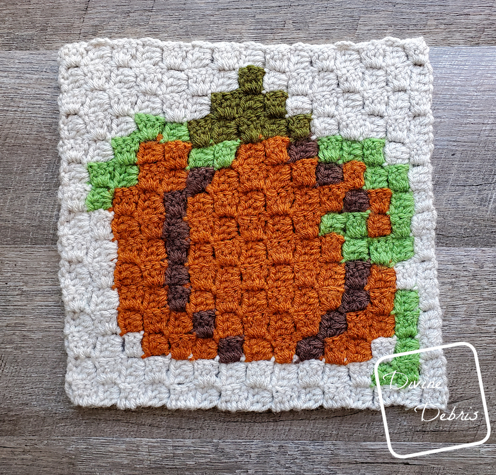 [Image description] The C2C Fall Pumpkin Afghan Square lays on a wood grain background.
