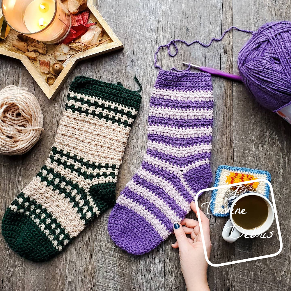 [Image description] The unfinished Alix Stocking and Odette Stocking crochet patterns lay on a wood grain background with a candle tray to the top left and yarn on the sides.