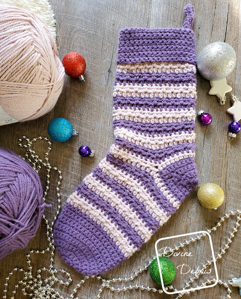 [Image description] the Striped Alix Stocking crochet pattern lays flat in the center of the photo with Christmas tree ornaments surrounding it