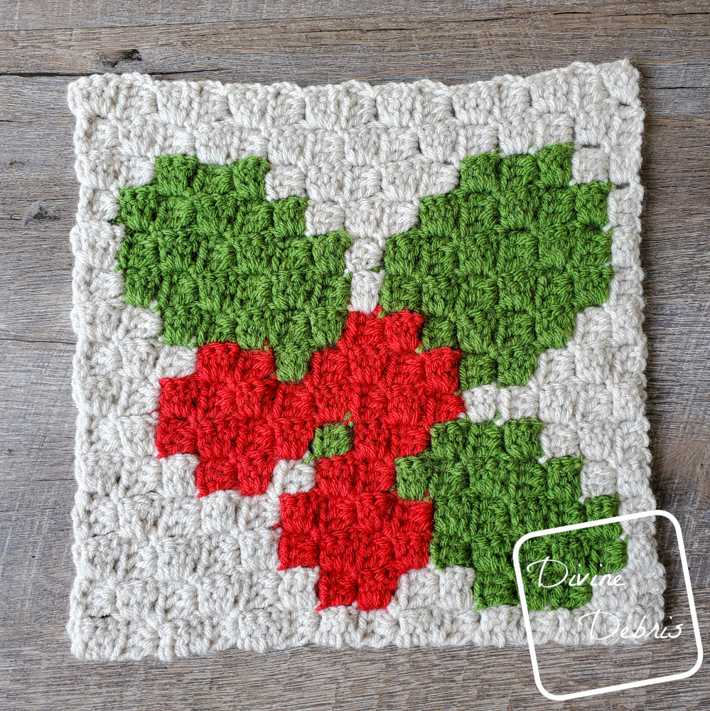 [Image description] The C2C Winter Holly Afghan Square lays on a wood grain background