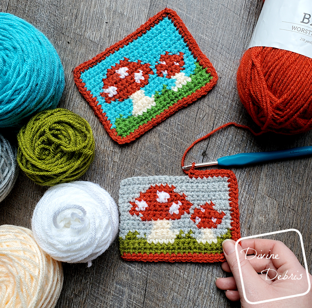 [Image description} 2 versions of the Cute Mushrooms Mug Rug lay flat on a wood grain background. One is in the process of getting a boarder and a white woman's hand holds the bottom corner