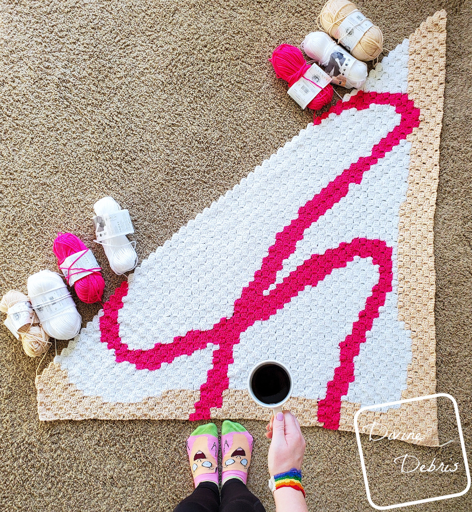 [Image description] A top down view of the half-done C2C Toaster Pastry Blanket, with a white woman's hand holding a cup of coffee and wearing socks.