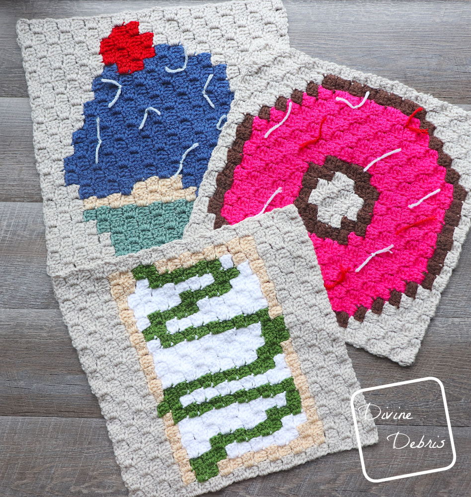 [Image description] A top down photo of the C2C Toaster Pastry Afghan Square, the C2C Donut Afghan Square, and C2C Cupcake Afghan Square on a fake wood background.