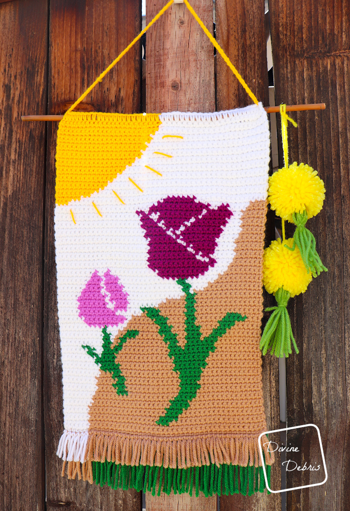 [Image description] The Cute Tulips Wall Hanging hangs against a fence