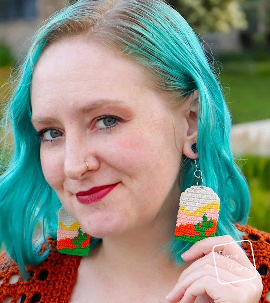 [Image description] A close up of the face of a white woman with blue hair wearing the Sedona Cactus Crochet Earrings.
