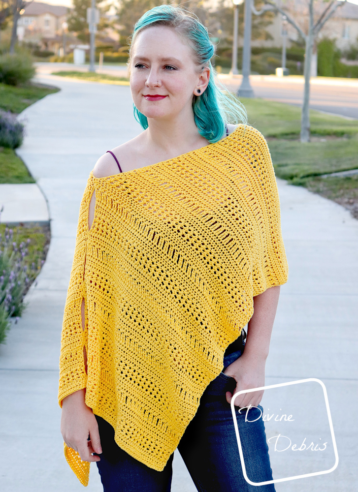 [Image description] A white woman with blue hair stands looking to the left from the camera on a sidewalk wearing the yellow Stephanie Poncho
