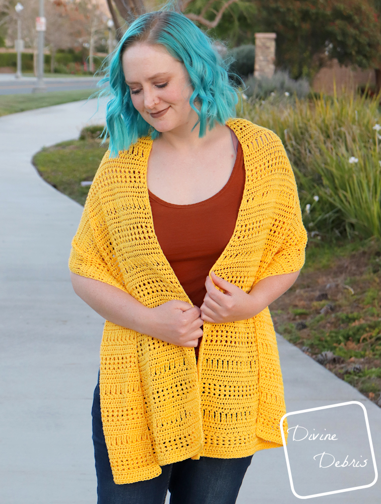 [Image description] A white woman with blue hair stands on a sidewalk wearing the yellow Stephanie Poncho long as a shawl