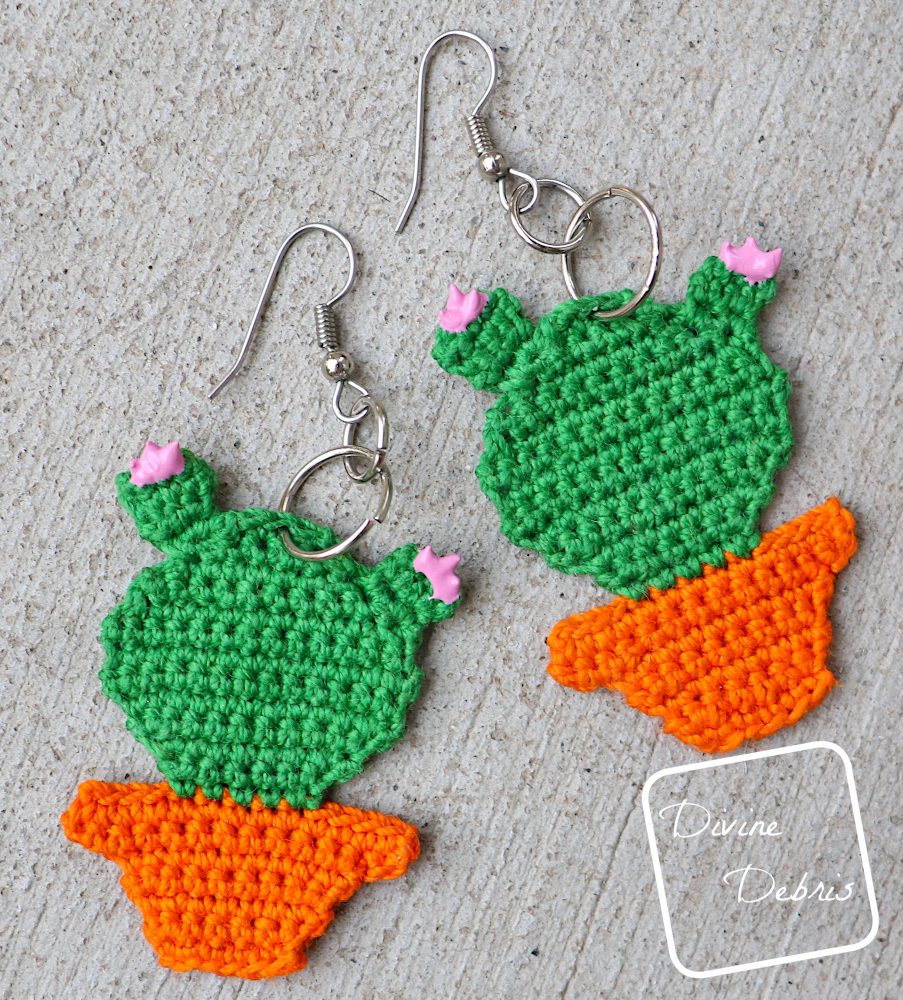 [Image description] A pair of the Cute Cactus Earrings lays flat on a cement background