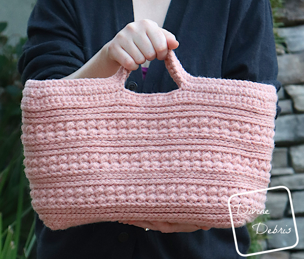 [Image description] A white woman, seen from the shoulders to the hips, is holding the soft pink Diana Basket with one had in the handles and another holding the base.