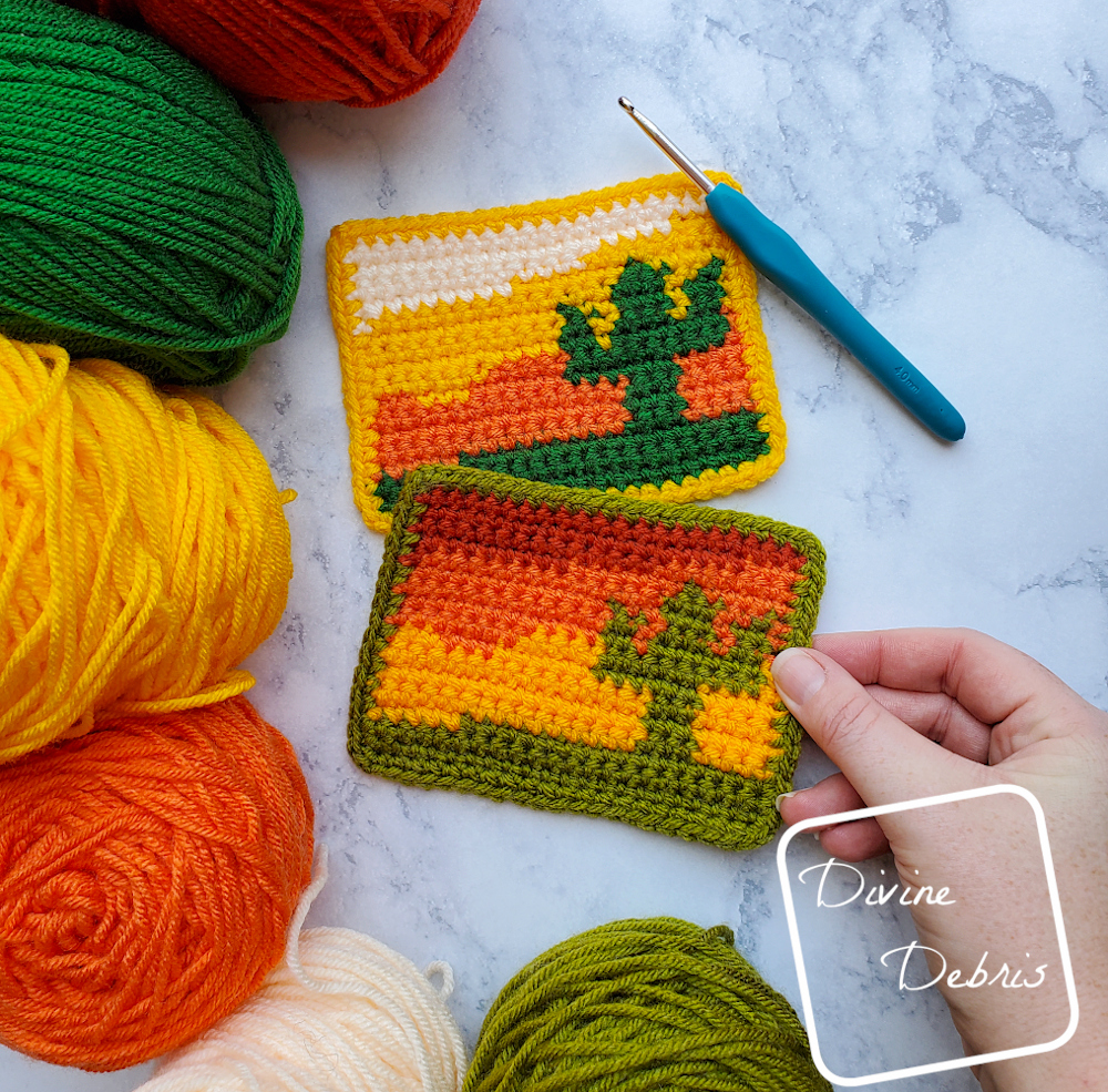[Image description] The 2 Sedona Cactus Mug Rugs laying flat on a fake white stone background with skeins of yarn on the left and a white woman's hand holding the bottom mug rug.
