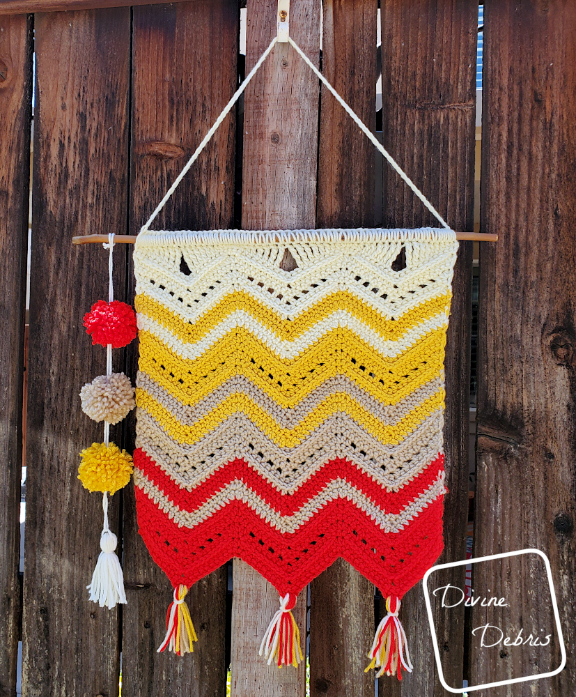 [Image description] The Colorful Chevrons Wall Hanging hangs on a hook on a fence.
