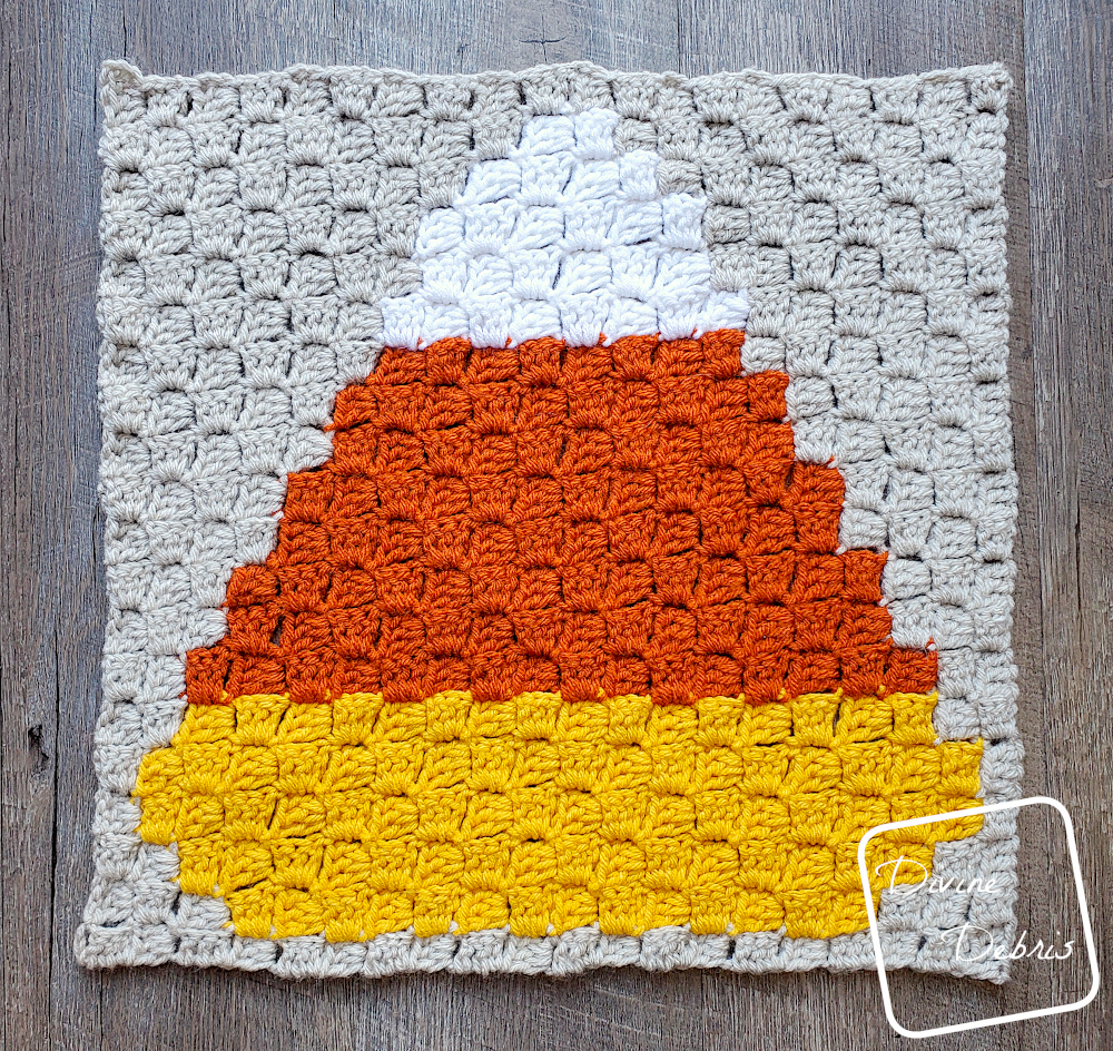 [Image description] A top down view of the C2C Candy Corn Afghan Square laying flat on a wood-grain background