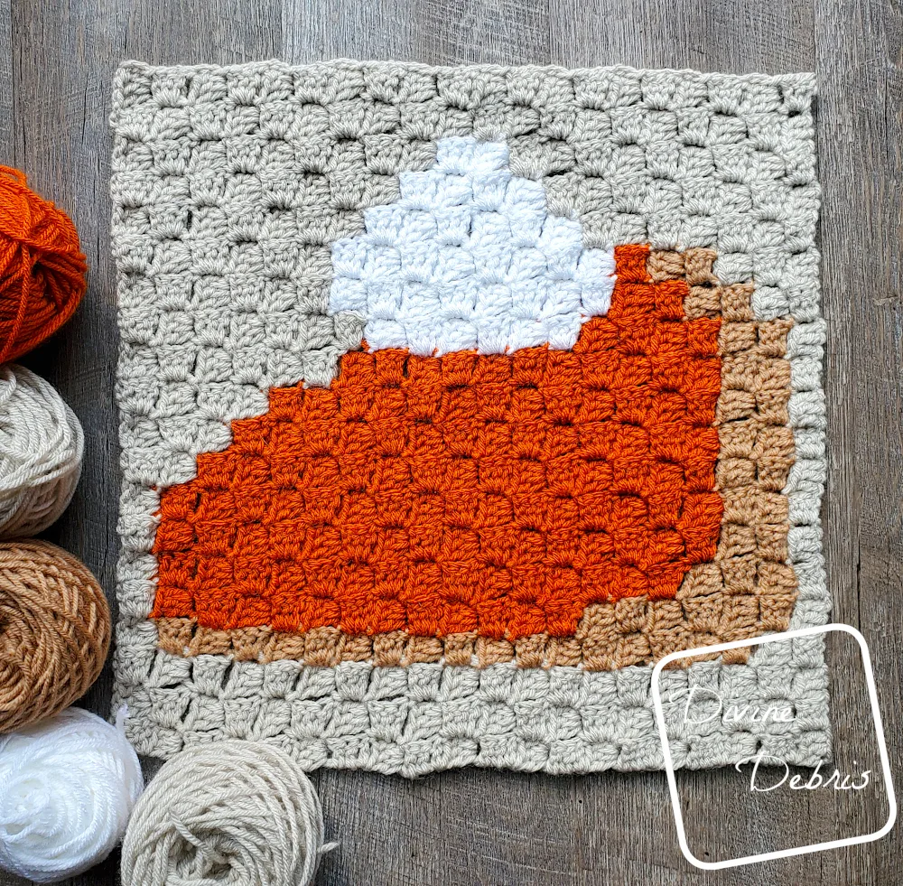[Image description] Top down view of the C2C Pumpkin Pie Square laying on a wood grain background, with skeins of yarn around the left side of the square.
