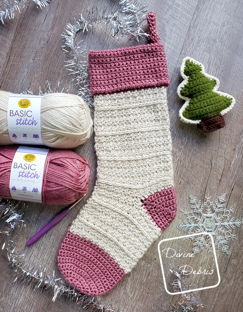 [Image description] Top down flat lay of the Kieran Stocking laying on a wood grain background, 2 skeins of yarn sit on the left, and Christmas decorations surround it. 