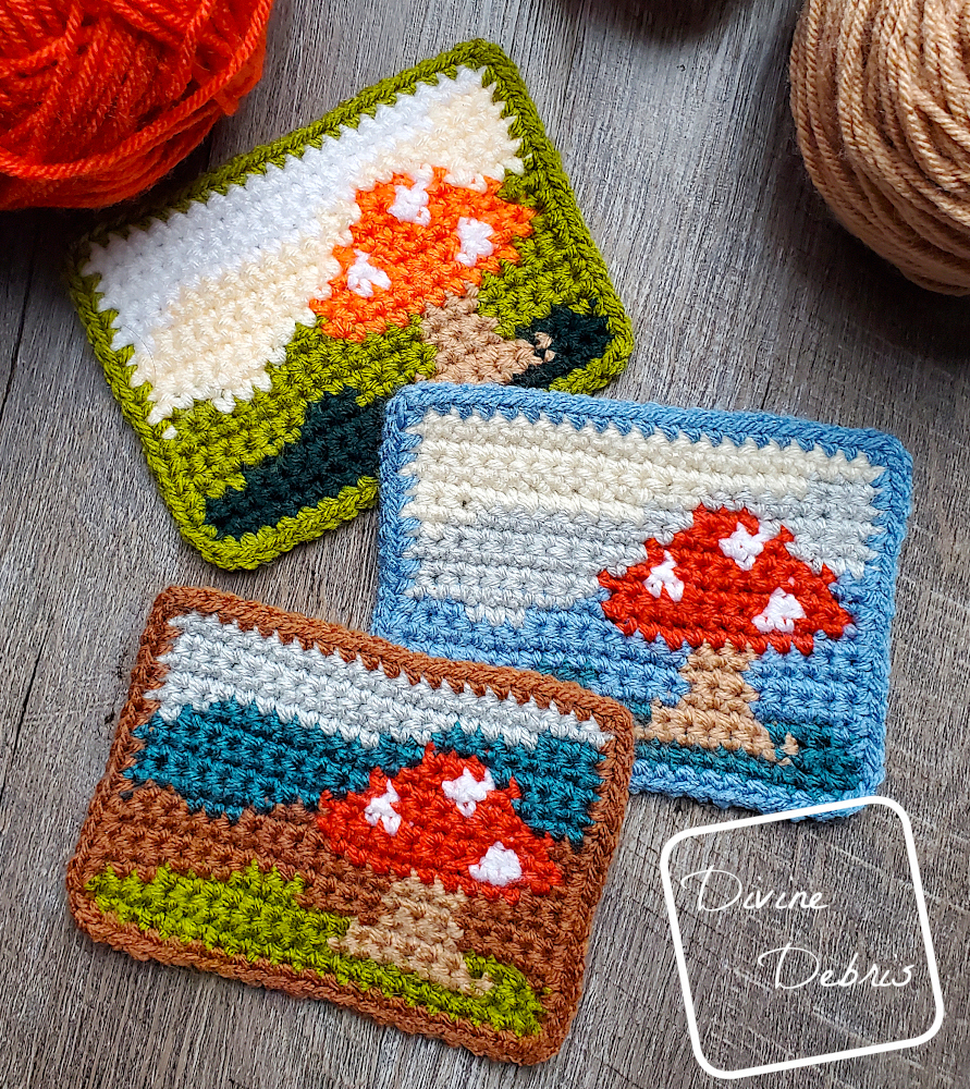 [Image description] Top down view of 3 Mushroom Landscape Mug Rugs on a wood grain background, 2 skeins of yarn can be seen at the top of the photo