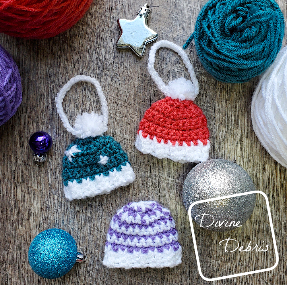 [Image description] Top down flat lay of three Winter Beanie Ornaments on a wood grain background, surrounded with Christmas ornaments and yarn
