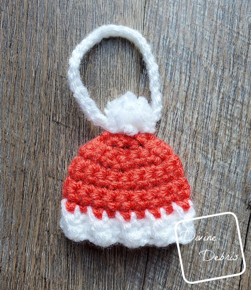 [Image description] Top down flat lay of a red Winter Beanie Ornament on a wood grain background