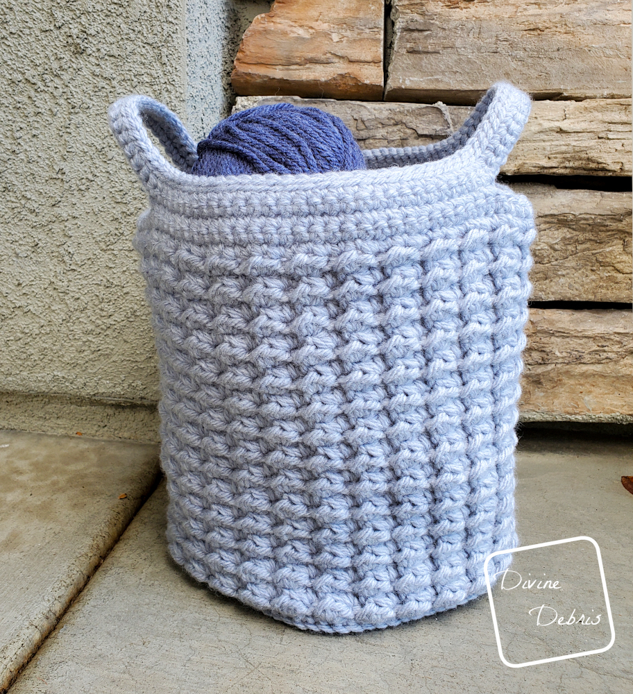 [image description] the Lucinda Basket crochet pattern made in light blue yarn sits in front of stone wall.