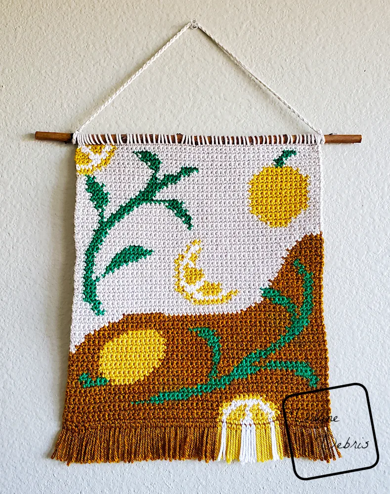[Image description] The Lovely Lemons Wall Hanging hanging on a tan wall.