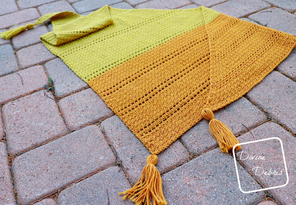 [Image description] The Kelsey Shawl lays flat on a reddish brick ground, at a angle to the camera