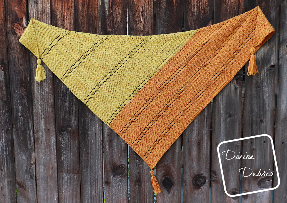 [Image description] The yellow and orange Kelsey Shawl hangs on a dark wood fence