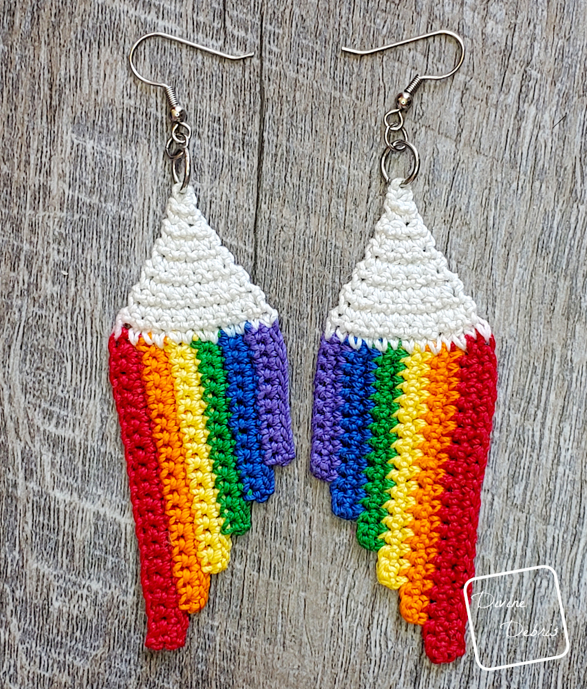 [Image description] Top down view of the Cascade Rainbow Earrings crochet pattern laying on fake wood background.