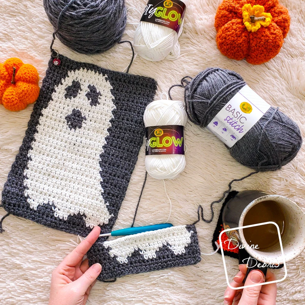 [image description] A top down view of a white woman's hand holding the bottom portion of the Gloria Ghost Scarf crochet pattern, with a finished ghost in the top left.