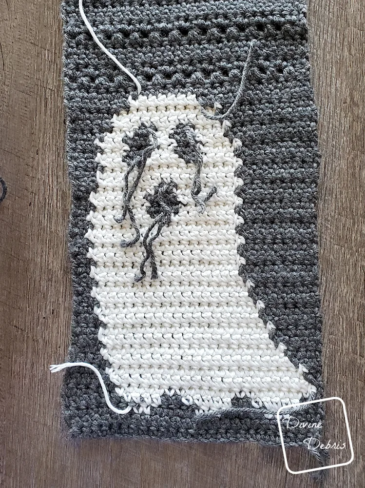 [Image description] Close up photo of using separate pieces of yarn for the eyes and mouth of the Gloria Ghost Scarf crochet pattern.