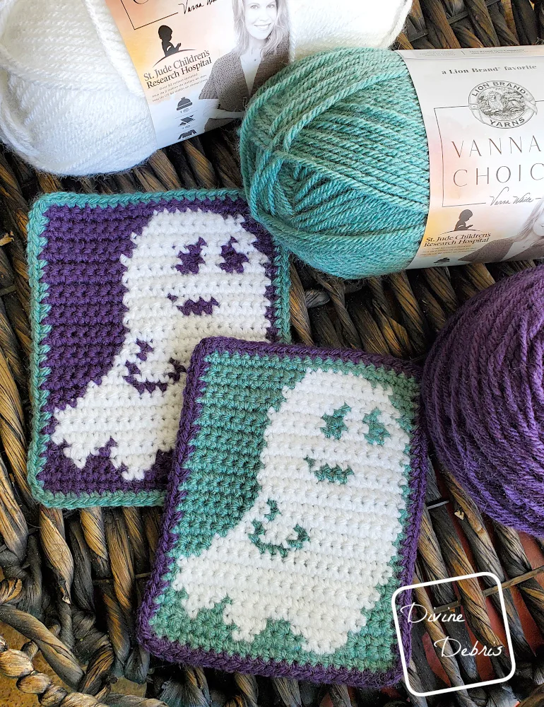 [Image description] Top down view of 2 Smiling Ghost Coaster on a wooden basket with skeins of yarn along the right side of the frame