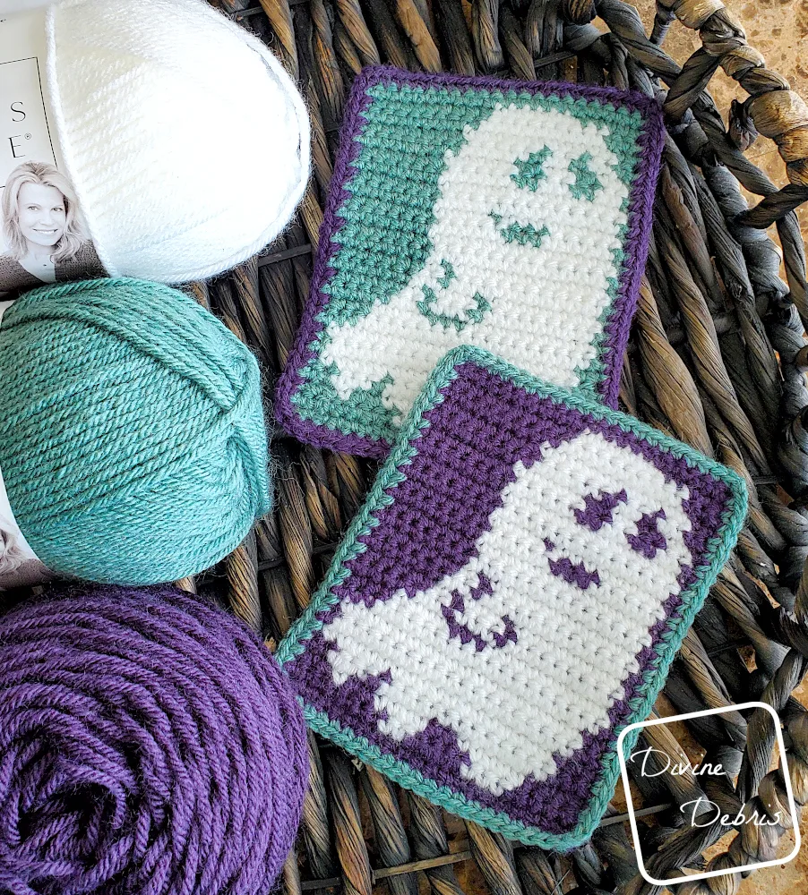 [Image description] Top down view of 2 Smiling Ghost Coaster on a wooden basket with skeins of yarn along the left side of the frame