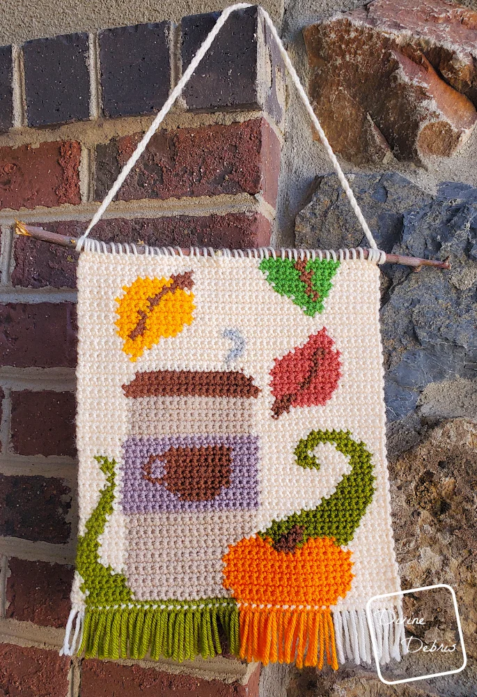 [Image description] The Fall Coffee Wall Hanging hangs on a corner of a stone wall.