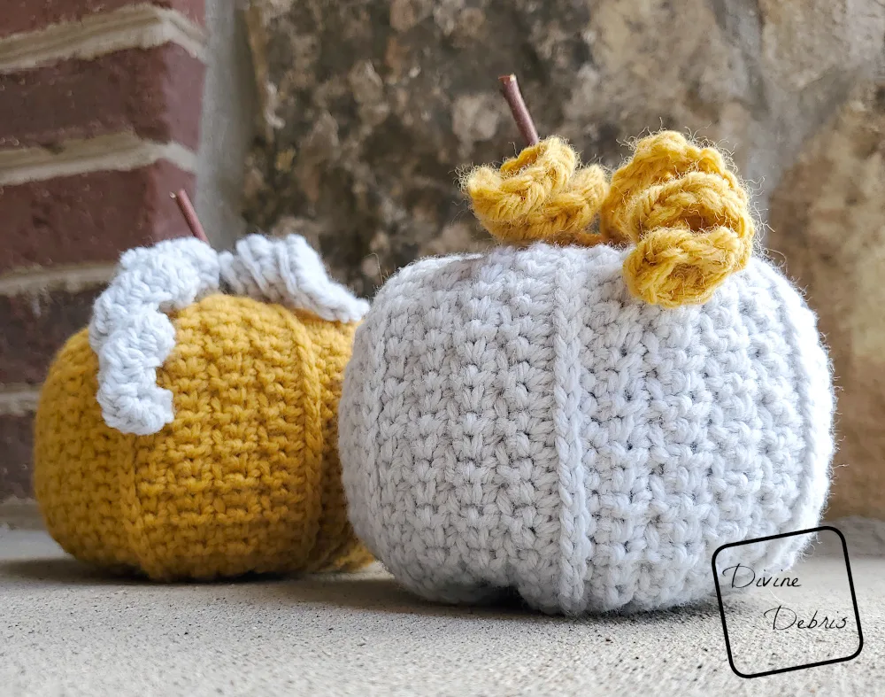 [Image description] a close up of 2 Keeley Pumpkins, one yellow and one gray, sitting on a cement ground against a brick wall