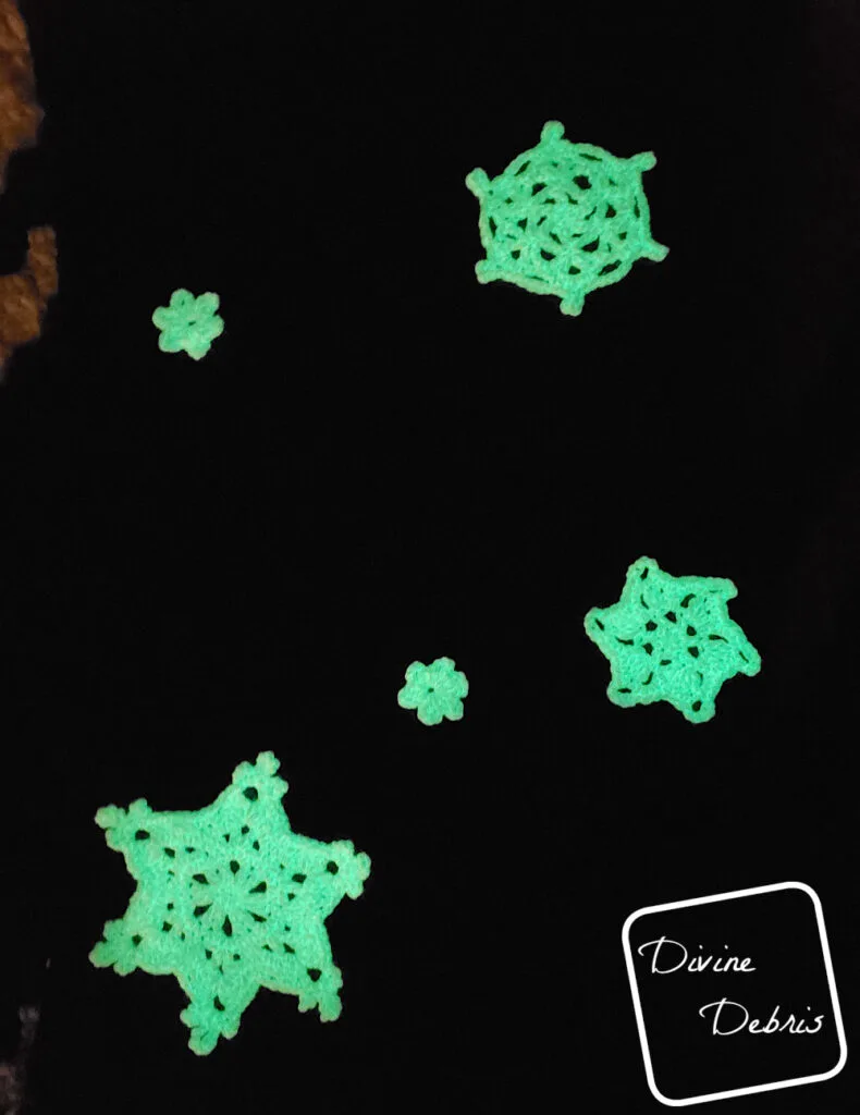 [Image description] A dark photo showing the snowflakes of the Crystal Snowflakes Shawl crochet pattern lit up glow in the dark.