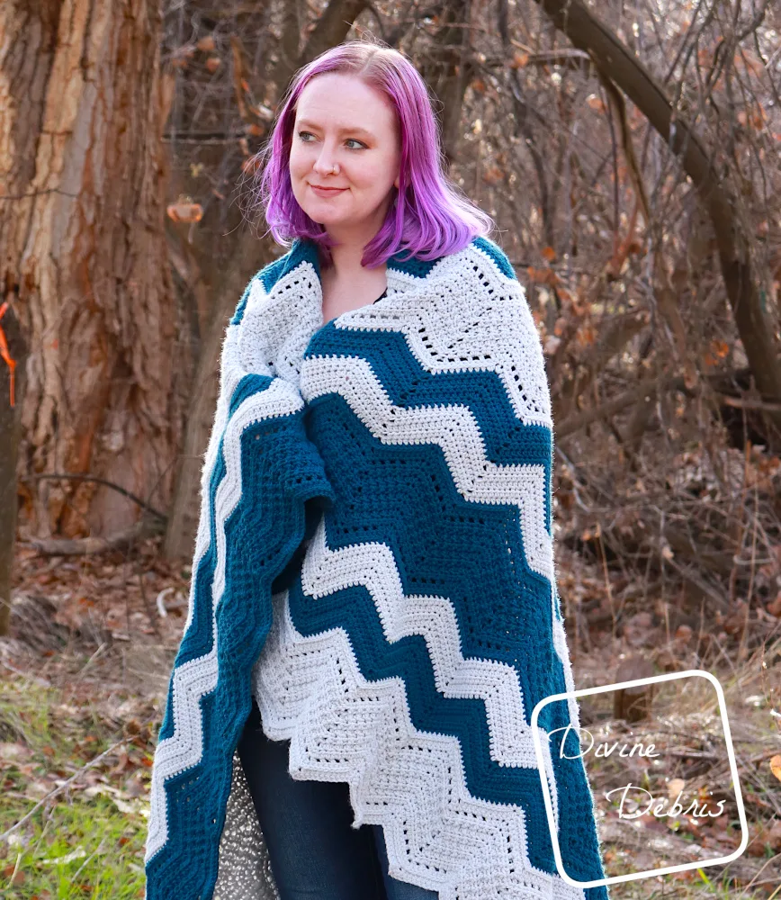 [image description] A white woman with purple hair stands in front of trees looking to her right with the Colorful Chevrons Blanket wrapped around her shoulders.