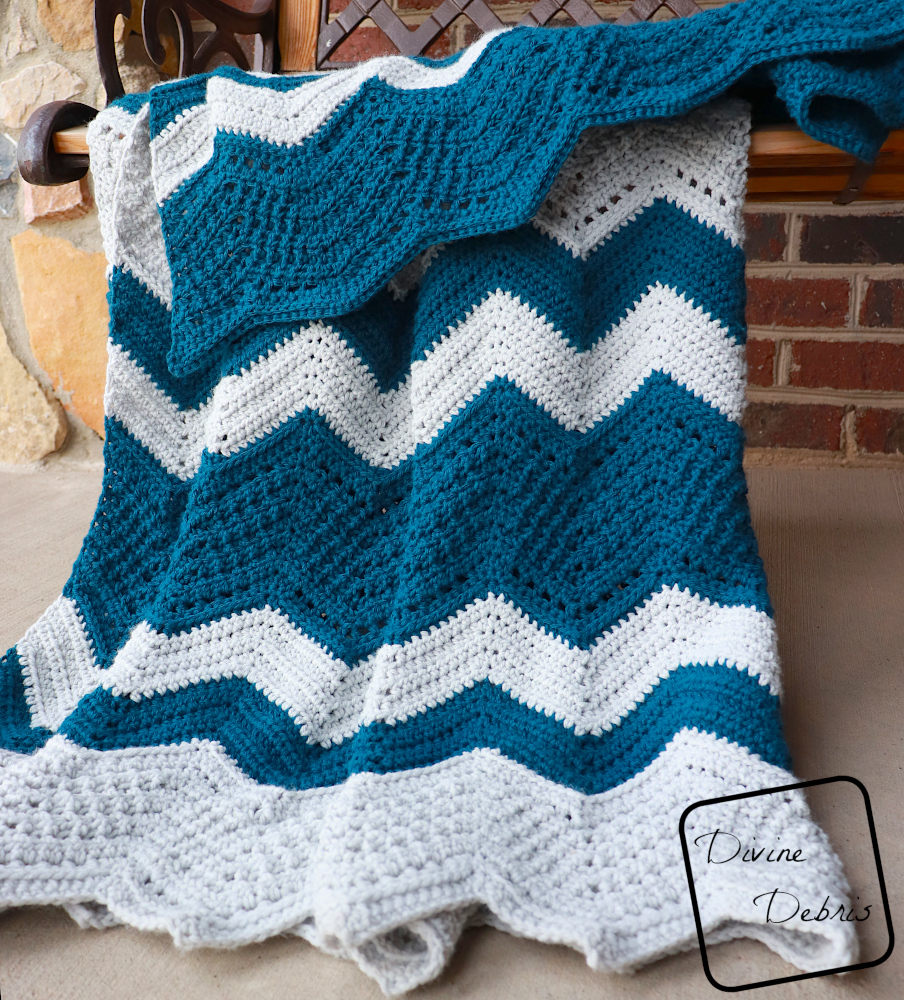 [image description] close up of the Colorful Chevrons Blanket hanging off a bench in front of a brick wall. 