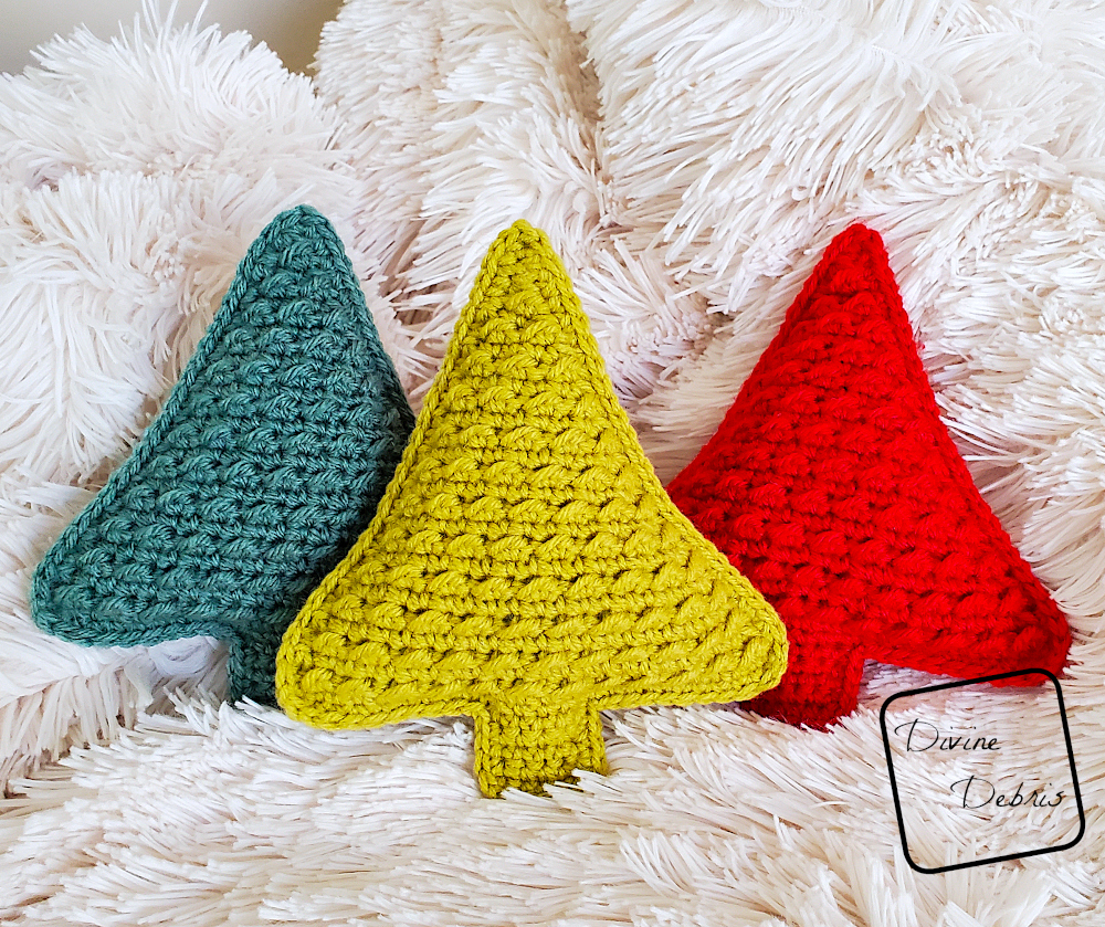 [Image description] 3 Cute Tree Amigurumis (one red, one lime green, and one sage green) stand up against a fuzzy white blanket.