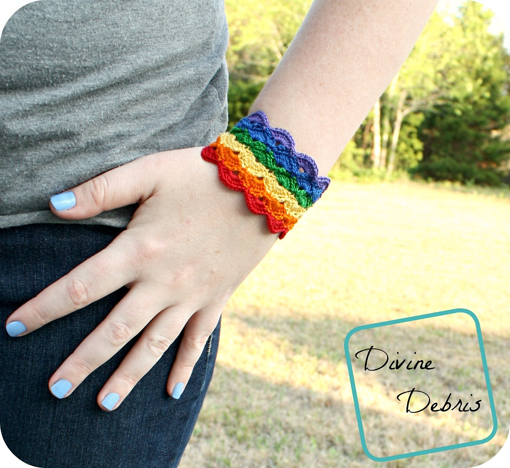 [image description] a close up photo of a white woman's wrist, hand, and arm while wearing the Janice Bracelet in rainbow colors in front of a lawn and trees.