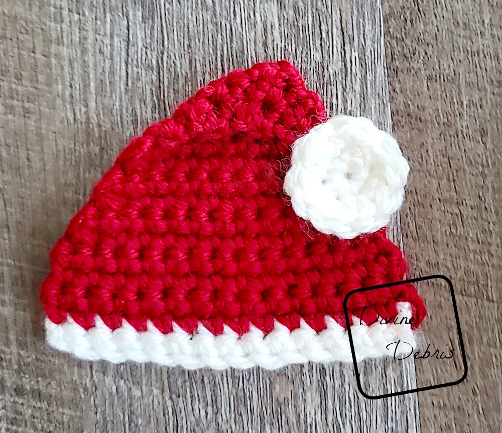 [Image description] Top down look at a finished Santa Hat Applique in red and white laying on a fake wood background.