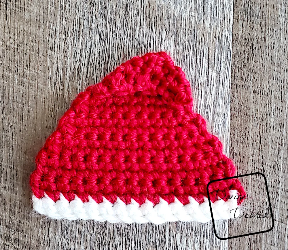 [Image description] Top down look at a unfinished red Santa Hat Applique laying on a fake wood background.